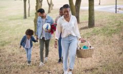 A joyful family walking in a park, carrying a picnic basket and a ball on a sunny day.